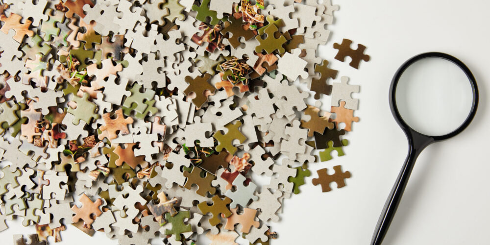 top view of magnifying glass and jigsaw puzzle pieces on grey top view of magnifying glass and jigsaw puzzle pieces on grey