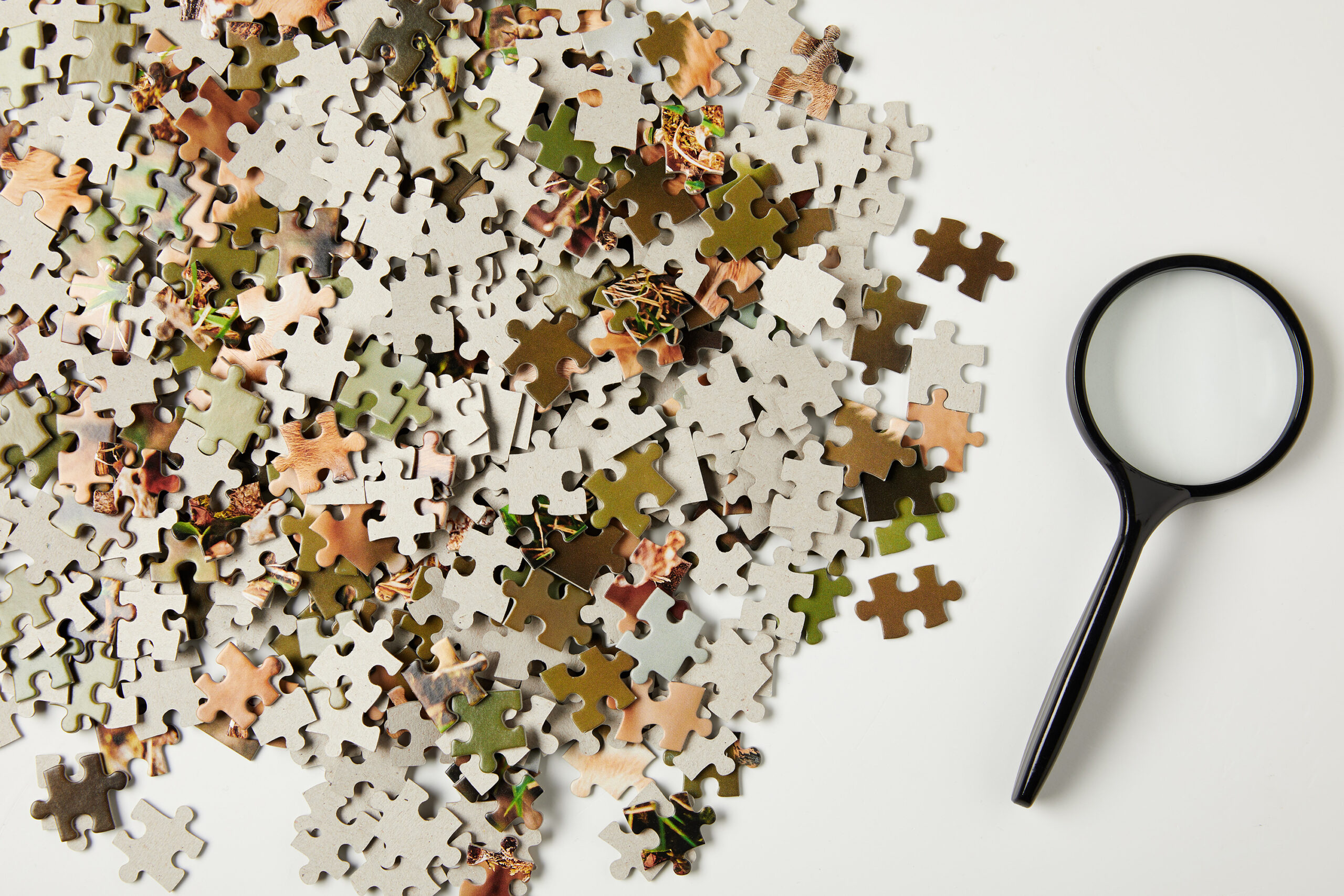top view of magnifying glass and jigsaw puzzle pieces on grey